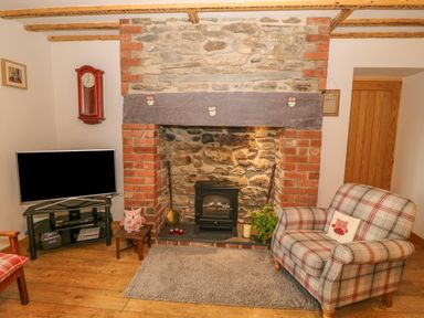 A sitting area with a plaid armchair a stone and brick fireplace a wall clock and a television at Caer Moel in Caernarfon