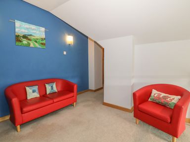 A room with a red sofa and red armchair with cushions and a blue wall with a painting at Caer Moel in Caernarfon
