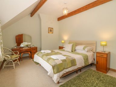 A bedroom with a double bed green and white bedding wooden nightstands with lamps a dressing table with mirror and a wicker chair at Caer Moel in Caernarfon