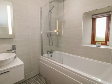 A bathroom with a bathtub and shower next to a window with a small plant on the sill at Caer Moel in Caernarfon