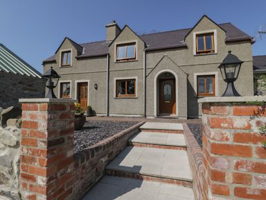 The front entrance of a stone house with stairs and brick pillars with lanterns at Caer Moel in Caernarfon