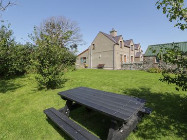 A garden with a black picnic table grass trees and a stone house with a green roof at Caer Moel in Caernarfon