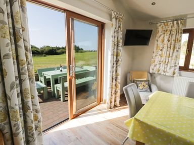 A dining area with a yellow polka dot tablecloth and a chair near sliding glass doors leading to an outdoor green picnic table with benches at Caer Moel in Caernarfon