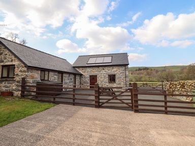 A stone barn with a gated driveway and solar panels on the roof at Beudy Bach Barn in Llanuwchllyn near Bala