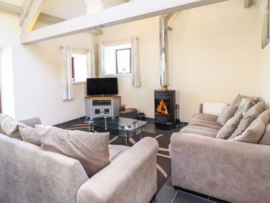 A living room with two sofas a glass coffee table a television and a wood burning stove at Beudy Bach Barn in Llanuwchllyn near Bala