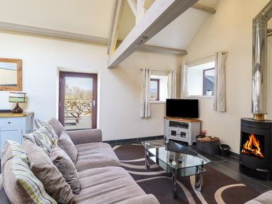 A living room with a sofa a glass coffee table a television a wood-burning stove and windows at Beudy Bach Barn Llanuwchllyn near Bala