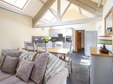 A kitchen and dining area with wooden table and chairs a sofa and a dresser with a lamp at Beudy Bach Barn in Llanuwchllyn near Bala