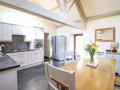 A kitchen and dining area with wooden table chairs flowers on table and kitchen appliances at Beudy Bach Barn in Llanuwchllyn near Bala