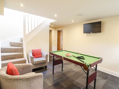 A room with a pool table a wall-mounted television two armchairs with red cushions and a carpeted staircase at Beudy Bach Barn in Llanuwchllyn near Bala