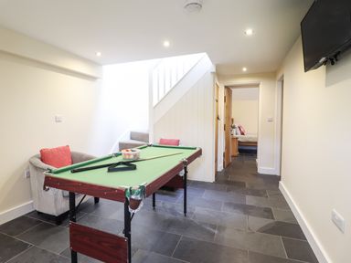 A room with a small pool table two armchairs a television on the wall and a bedroom visible through a doorway at Beudy Bach Barn in Llanuwchllyn near Bala