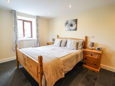 A bedroom with a wooden bed and bedside tables next to a window with curtains at Beudy Bach Barn in Llanuwchllyn near Bala