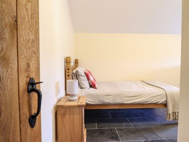 A bedroom with a wooden bed frame a side table and a lamp at Beudy Bach Barn in Llanuwchllyn near Bala