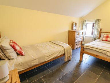 A bedroom with two single beds a wooden chest of drawers and a window with curtains at Beudy Bach Barn in Llanuwchllyn near Bala