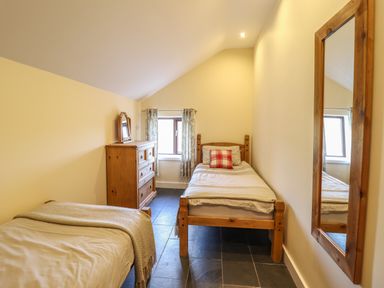 A bedroom with two single beds a wooden dresser a window with curtains and a wall mirror at Beudy Bach Barn in Llanuwchllyn near Bala