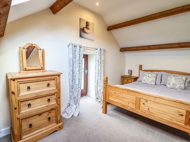 A bedroom with wooden bed and dresser and curtains on a door at Beudy Bach Barn in Llanuwchllyn near Bala
