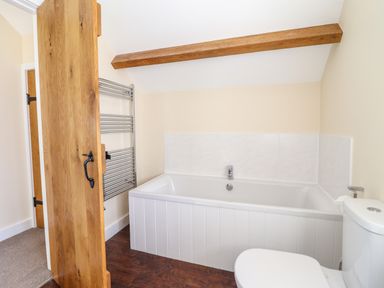 A bathroom with a bathtub a toilet a wooden door and a heated towel rail at Beudy Bach Barn in Llanuwchllyn near Bala