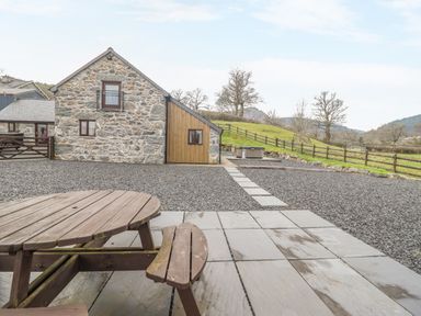 An outdoor area with a wooden picnic table gravel ground stone path and a stone building with wooden panel at Beudy Bach Barn in Llanuwchllyn near Bala