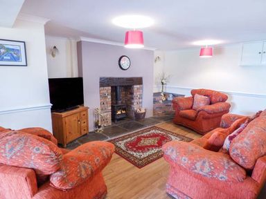 A living room with orange patterned sofas a television on a wooden stand a brick fireplace and a red patterned rug at Arfryn in Bethesda