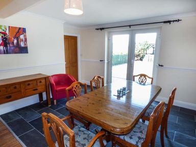 A dining room with a wooden table and chairs a red armchair a wooden sideboard and glass doors at Arfryn in Bethesda
