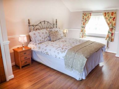 A bedroom with a double bed bedside tables with lamps and floral curtains at Arfryn in Bethesda
