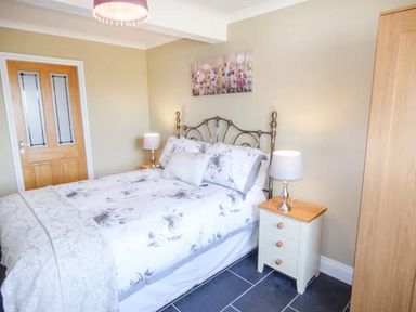 A bedroom with a double bed and floral bedding a wooden door a bedside table with a lamp and a wooden wardrobe at Arfryn in Bethesda