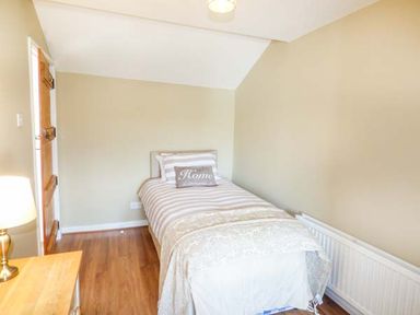 A bedroom with a single bed a wooden door a lamp on a small table and a radiator at Arfryn in Bethesda