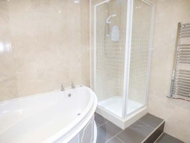 A bathroom with a white bathtub a glass shower enclosure and a heated towel rail at Arfryn in Bethesda