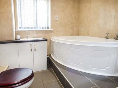A bathroom with a corner bathtub sink with cabinet and toilet at Arfryn in Bethesda