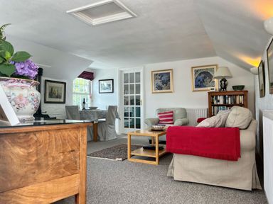 A living room with a beige sofa and armchair a wooden coffee table and a wooden sideboard with a flower vase at The Boat House in Golant near Tywardreath
