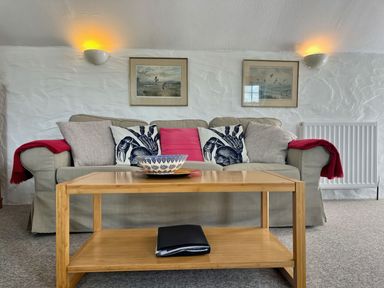 A sofa with cushions and red throws with a wooden coffee table in front of it at The Boat House in Golant near Tywardreath