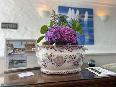 A ceramic vase with purple flowers on a wooden table with photo frame and papers in a room at The Boat House in Golant near Tywardreath