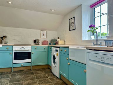 A kitchen with turquoise cabinets white appliances and a window with a view at The Boat House Golant near Tywardreath