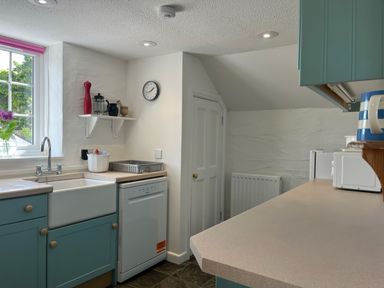 A kitchen with a sink dishwasher countertop cabinets and a window with flowers on the sill at The Boat House in Golant near Tywardreath