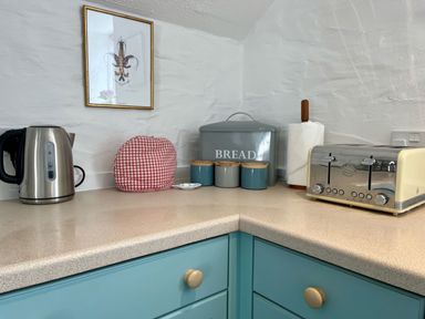 A kitchen counter with a kettle toaster bread box three jars paper towel and a framed lobster print at The Boat House in Golant near Tywardreath