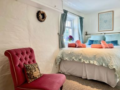 A bedroom with a bed with rolled towels on it a red chair and a window with curtains at The Boat House in Golant near Tywardreath