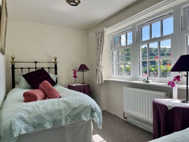 A bedroom with a single bed with striped bedding two rolled towels a bedside table with a lamp and flowers and a window showing an outdoor view at The Boat House in Golant near Tywardreath
