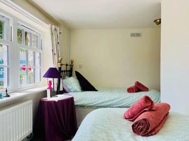 A bedroom with two single beds windows and a small table with a lamp at The Boat House in Golant near Tywardreath