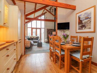A dining area with a wooden table set for six and a living room with sofas and large windows at The Wagon House in Tresmeer near Launceston