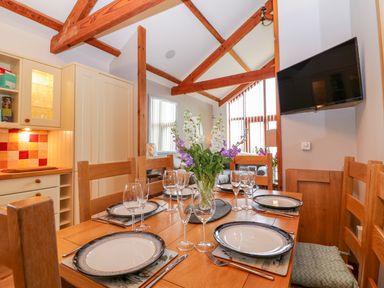A dining table set with plates glasses and cutlery in a room with wooden beams and a wall mounted tv at The Wagon House Tresmeer near Launceston