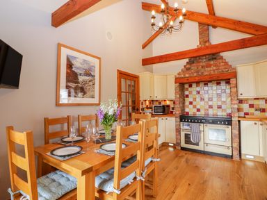 A kitchen with wooden dining table and chairs set with plates and glasses a stove with brick surround and tiled backsplash and wooden beams on ceiling at The Wagon House Tresmeer near Launceston