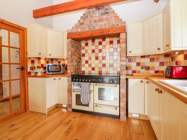 A kitchen with tiled backsplash cream cabinets wooden countertop and a black and cream oven at The Wagon House Tresmeer near Launceston