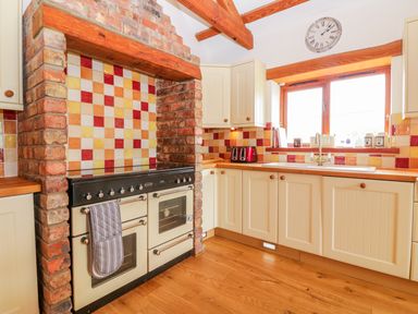 A kitchen with a stove under a brick arch and tiled backsplash at The Wagon House in Tresmeer near Launceston
