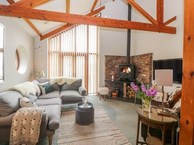 A living room with a grey sectional sofa wood burner and a glass table with flowers at The Wagon House in Tresmeer near Launceston