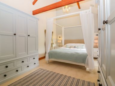 A bedroom with a four-poster bed a wardrobe and a striped rug at The Wagon House in Tresmeer near Launceston