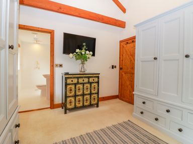 A bedroom with a patterned dresser with flowers on top a wall mounted TV wardrobe and a door leading to a bathroom at The Wagon House in Tresmeer near Launceston