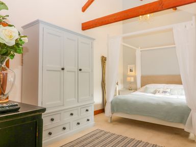 A bedroom with a four-poster bed, wardrobe, mirror, and wooden ceiling beams at The Wagon House in Tresmeer near Launceston