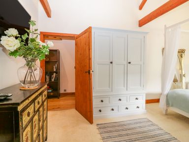 A bedroom with a tall light wardrobe a wooden door a chest with a vase of flowers and a striped rug at The Wagon House Tresmeer near Launceston