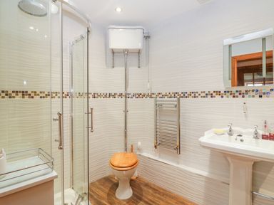 A bathroom with a glass shower enclosure toilet with a wooden seat pedestal sink and a mirror at The Wagon House Tresmeer near Launceston