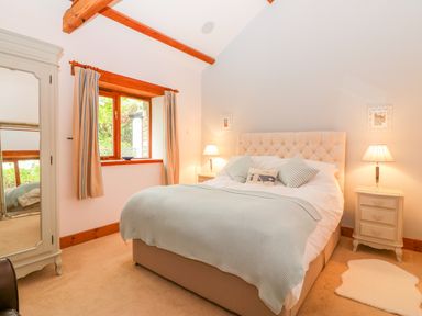 A bedroom with a bed a beige headboard two bedside tables with lamps a window with curtains a wardrobe with mirror and a beige carpet at The Wagon House Tresmeer near Launceston