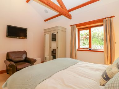 A bedroom with a bed a leather armchair a wardrobe a wall-mounted television and a window with curtains at The Wagon House Tresmeer near Launceston